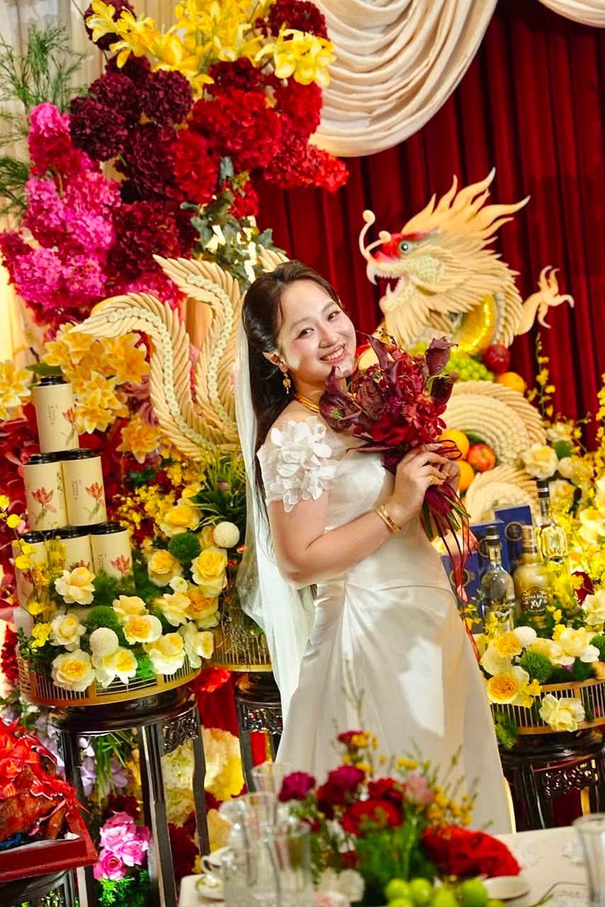 Cô dâu váy trắng cầm hoa đỏ trước tráp rồng phượng
