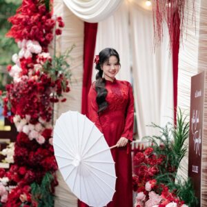 Cô dâu áo dài đỏ bên trụ hoa đỏ lối vào rạp lễ ăn hỏi tại nhà