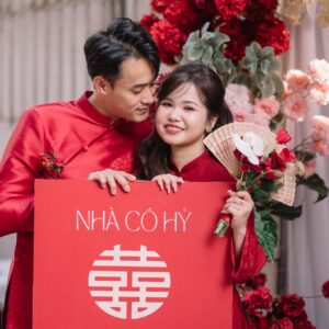 Cô dâu chú rể áo dài đỏ cầm bảng Nhà có hỷ trong lễ ăn hỏi tại nhà