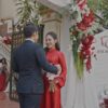 Cô dâu áo dài đỏ chú rể trước cổng cưới hoa hồng đỏ