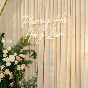 Backdrop neon đám cưới Phương Hà Hồng Lâm neon trắng ấm rèm kem hoa trắng hồng