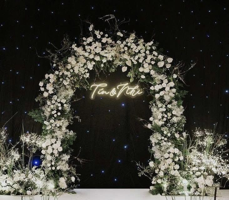 Backdrop neon đám cưới Tín Nhi neon vàng giữa vòm hoa trắng phông sao đen