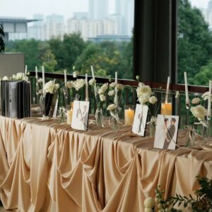 Bàn đón khách khăn satin champagne ảnh cưới nến hoa trắng view thành phố