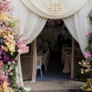 Bảng nhà có hỷ trắng chữ đen viết tay Phương Anh Đức Minh dưới trụ hoa pastel cổng vải trắng
