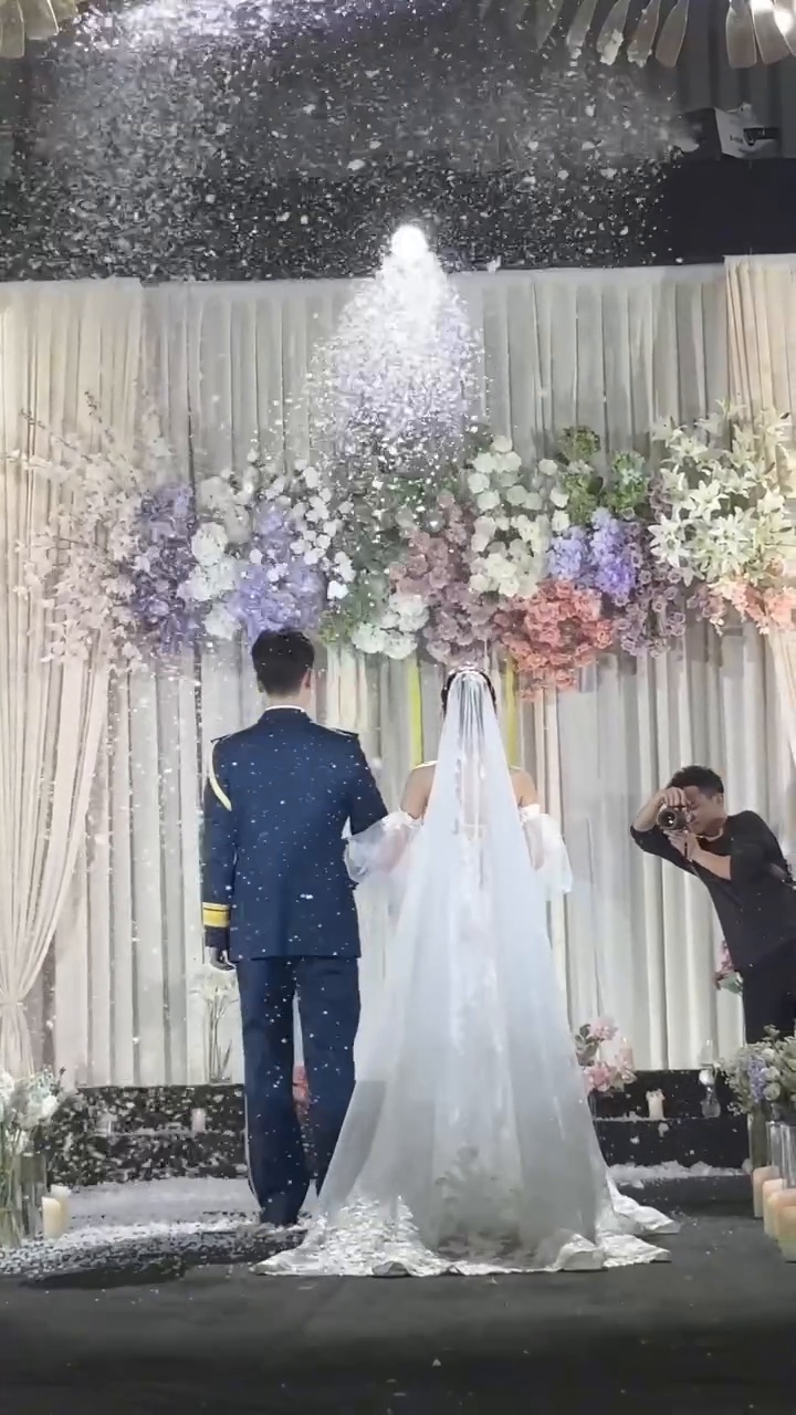 Cặp đôi đứng giữa sân khấu rèm trắng cổng hoa tím pháo giấy bắt đầu rơi nhiếp ảnh gia