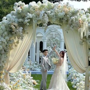 Cặp đôi dưới cổng hoa cưới ngoài trời vòm hoa trắng dãy cột La Mã