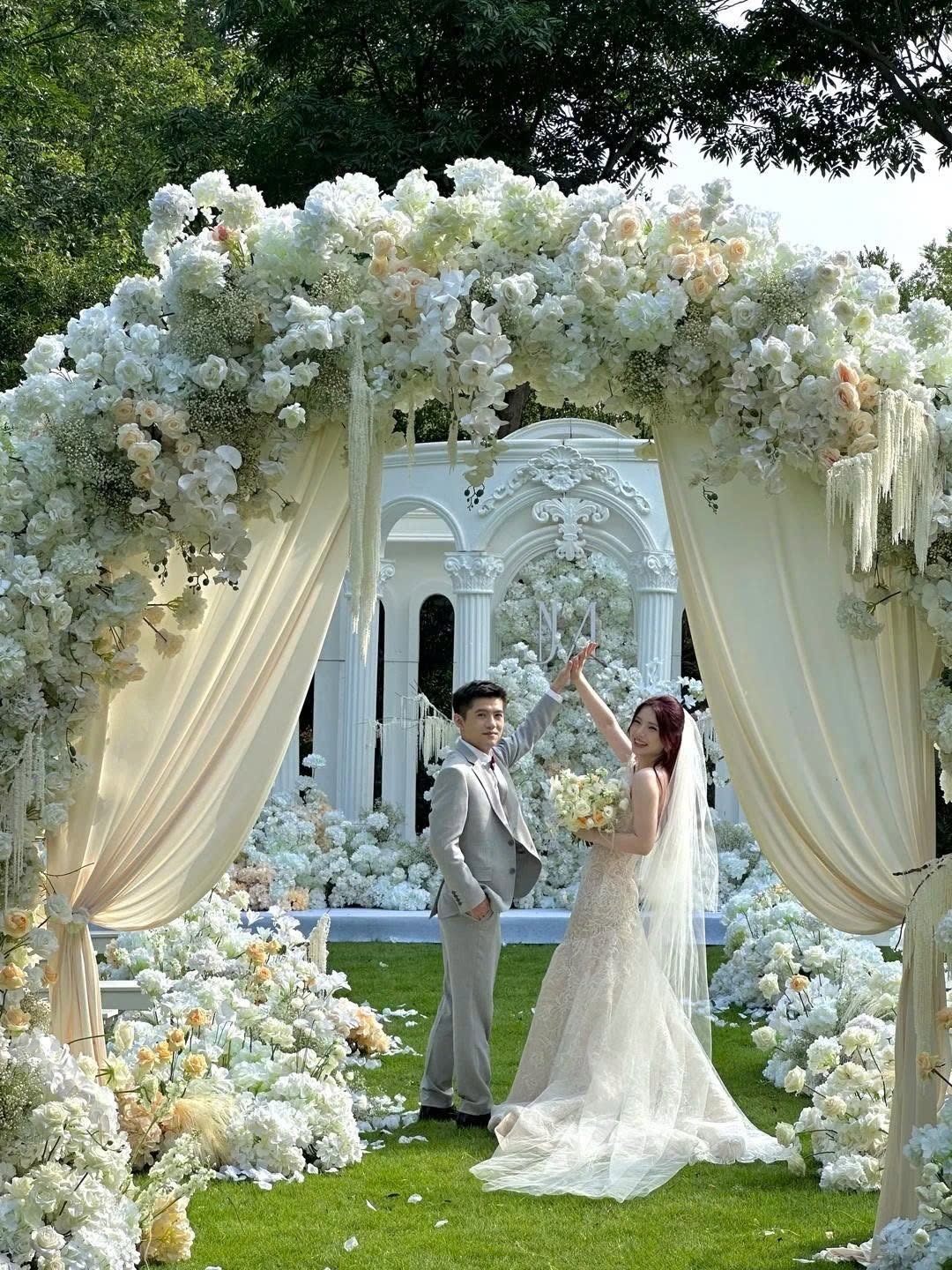 Cặp đôi dưới cổng hoa cưới ngoài trời vòm hoa trắng dãy cột La Mã