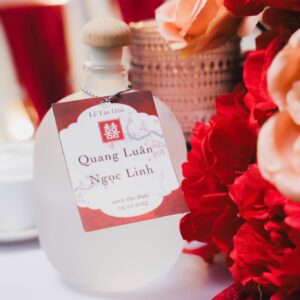 Chai thủy tinh thẻ đỏ in tên lễ tân hôn Quang Luân Ngọc Linh hoa hồng đỏ