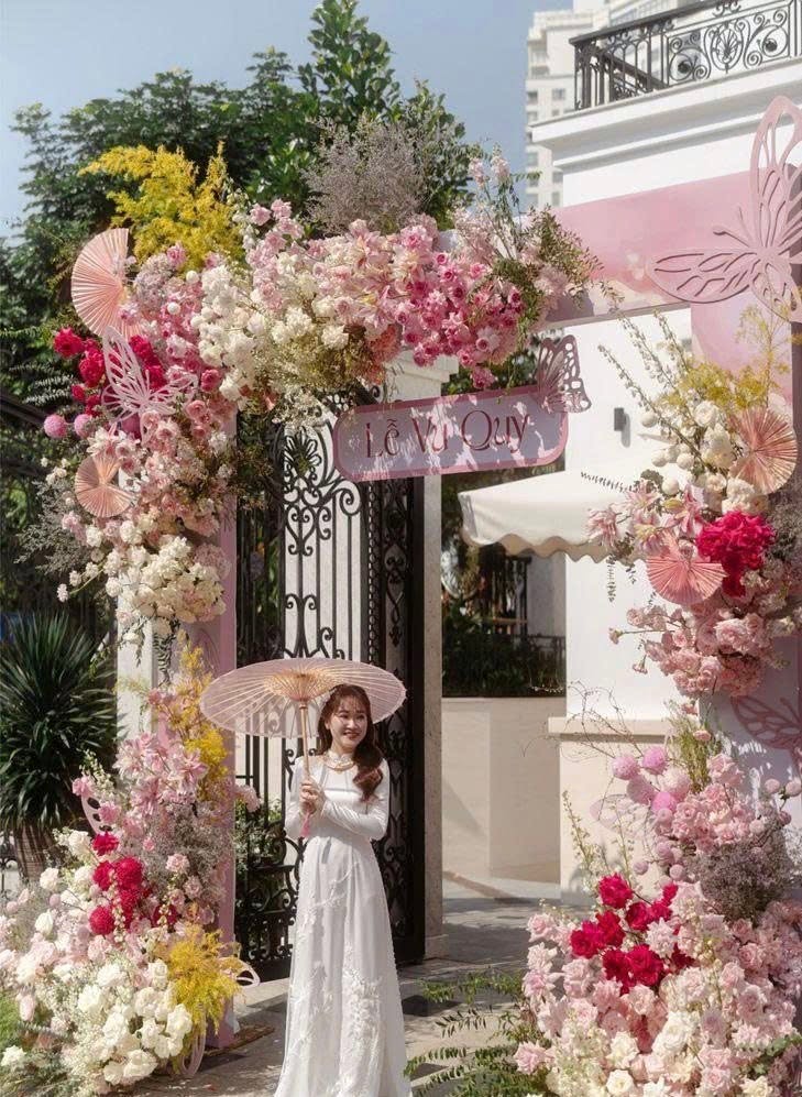 Chụp ảnh cô dâu áo dài ngày cưới cầm ô giấy giữa cổng hoa hồng trước biệt thự