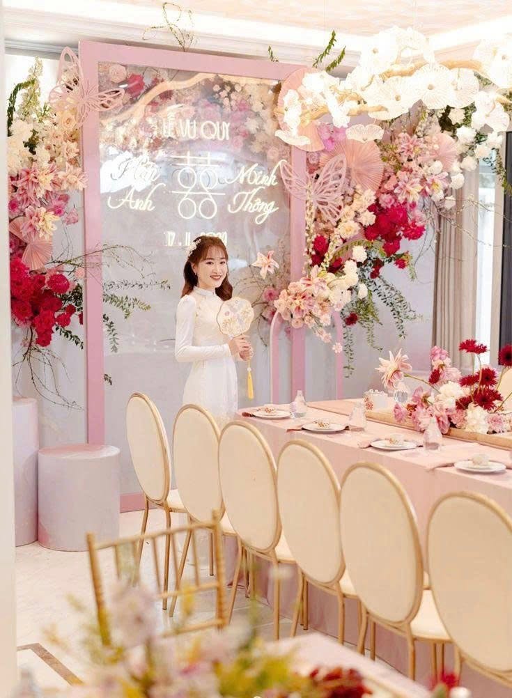 Chụp ảnh cô dâu áo dài ngày cưới cầm quạt bên bàn trà backdrop hồng cánh bướm lễ vu quy