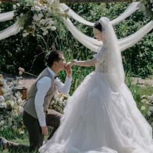 Chụp ảnh cưới ngoài trời chú rể quỳ hôn tay cô dâu dưới vòm tre voan trắng