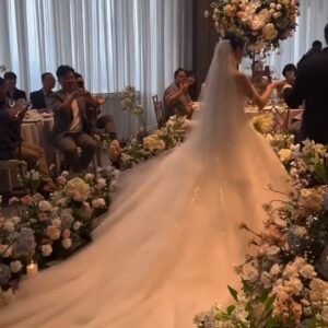Cô dâu váy đuôi dài bước trên lối hoa cam đào xanh giữa sảnh khách sạn khách mời