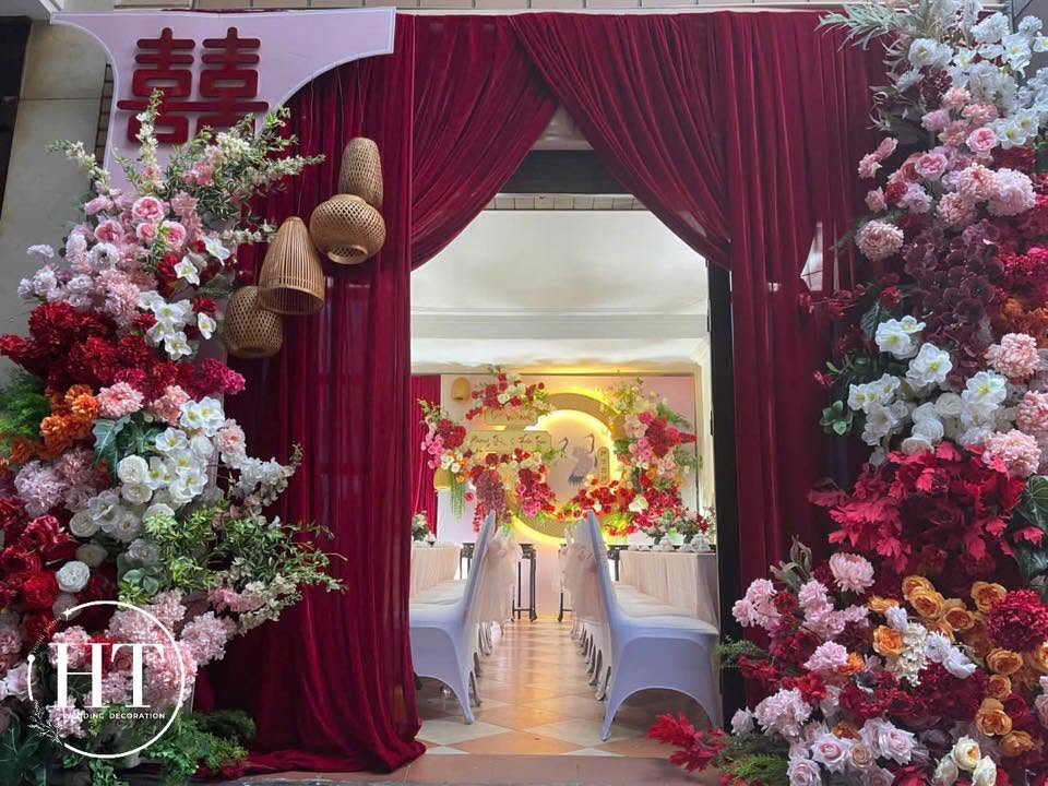 Cổng rèm nhung đỏ vén đèn mây chữ hỷ hoa hồng trắng đỏ cam nhìn vào sảnh tiệc