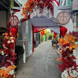 Cổng vòm trắng chữ Vu Quy chữ hỷ tròn hoa cam đỏ đầu ngõ nhỏ