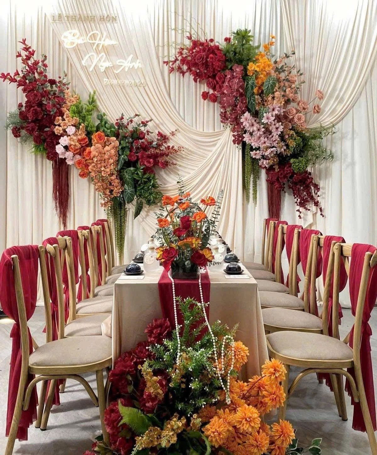 Lễ thành hôn Bùi Hân Ngọc Anh backdrop vải kem rủ hoa đỏ cam bàn trà dài ghế gỗ voan đỏ