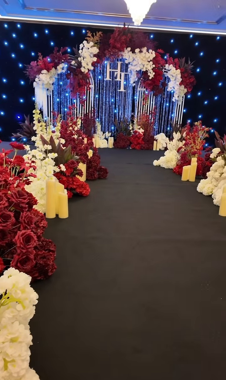 Lối đi thảm đen hoa đỏ đô trắng ngà nến trụ dẫn lên sân khấu sảnh cưới tone đỏ