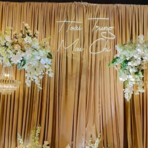 Mẫu backdrop cưới đẹp rèm champagne hoa trắng tên neon Hoài Trung Mai Chi