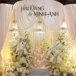 Mẫu backdrop cưới đẹp rèm kem vén đèn chùm pha lê bậc nến hoa trắng Hải Đăng Minh Anh