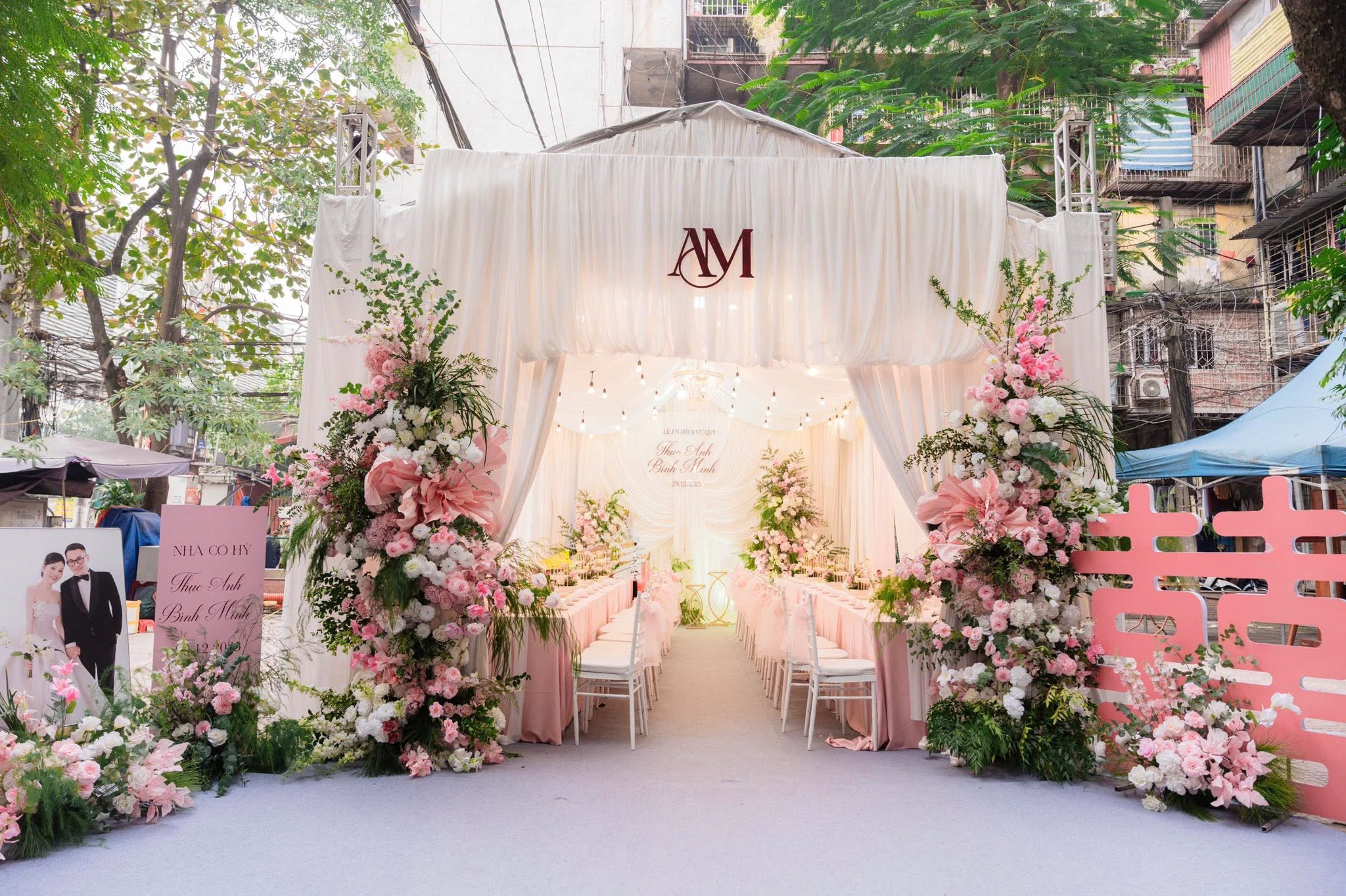 Mẫu cổng hoa cưới đẹp rạp trắng mái vòm monogram AM trụ hoa hồng pastel chữ hỷ hồng mặt phố