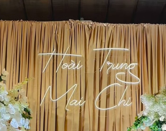 Neon tên viết tay Hoài Trung Mai Chi trên rèm nhung champagne sảnh cưới