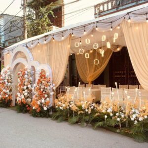 Rạp cưới tông cam đào ngoài phố vòm trắng nhiều lớp đèn treo luống hoa thấp