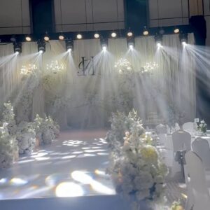 Sân khấu tiệc cưới đèn beam sảnh trắng monogram rèm voan trắng gobo hoa văn lối đi hoa trắng