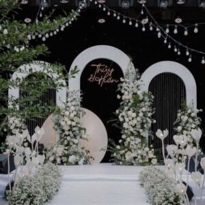Sân khấu vòm trắng neon tên Thùy Hiền đèn hoa tulip trắng hoa baby bậc trắng dây bóng đèn