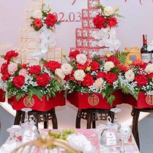 Tráp lục giác đỏ chữ Hỷ vàng cắm hoa hồng đỏ lan trắng đặt trên đôn gỗ lễ vu quy Phương Nhi Minh Nhật