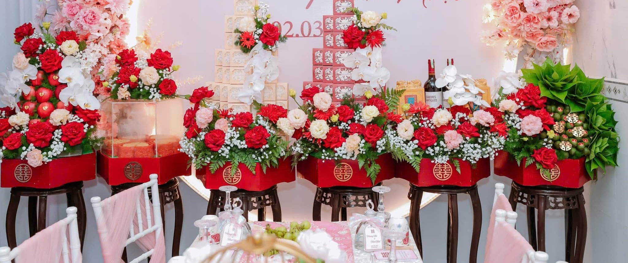 Tráp lục giác đỏ chữ Hỷ vàng cắm hoa hồng đỏ lan trắng đặt trên đôn gỗ lễ vu quy Phương Nhi Minh Nhật