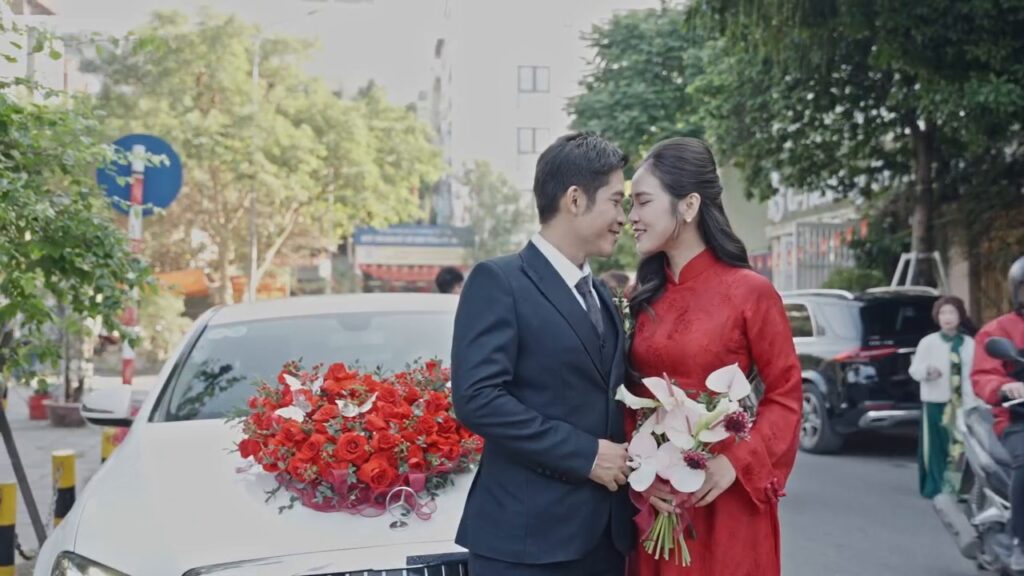 Cô dâu áo dài đỏ cầm hoa cầm tay trắng bên xe hoa