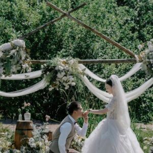 Vòm tre chéo voan trắng cụm hoa trắng xanh chú rể quỳ cổng hoa cưới ngoài trời vườn
