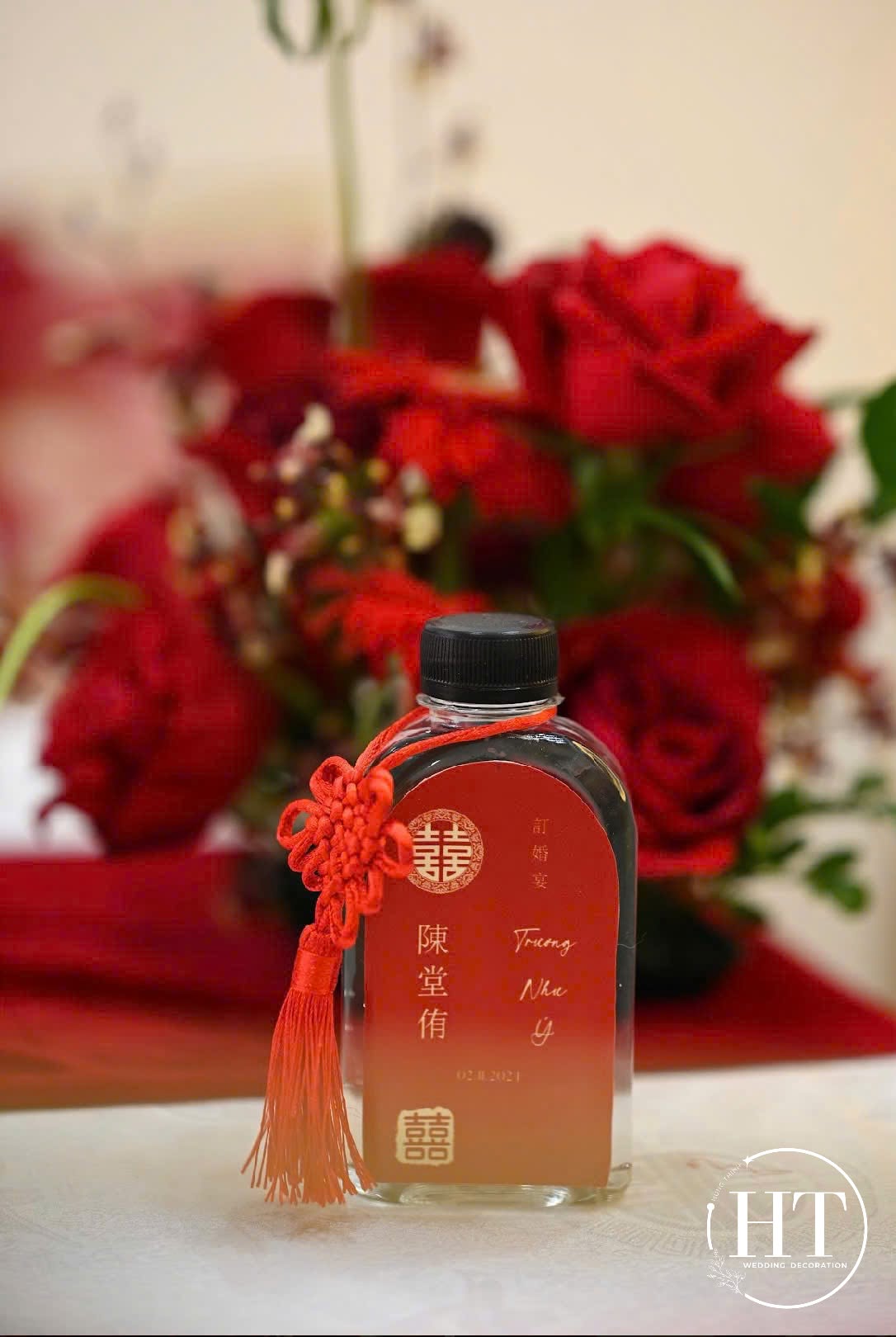Chai rượu tag đỏ cắm hoa hồng đỏ trên bàn tiếp khách trong lễ vu quy